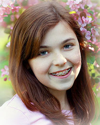 young teenage girl with braces smiling and standing in front of a blossom tree